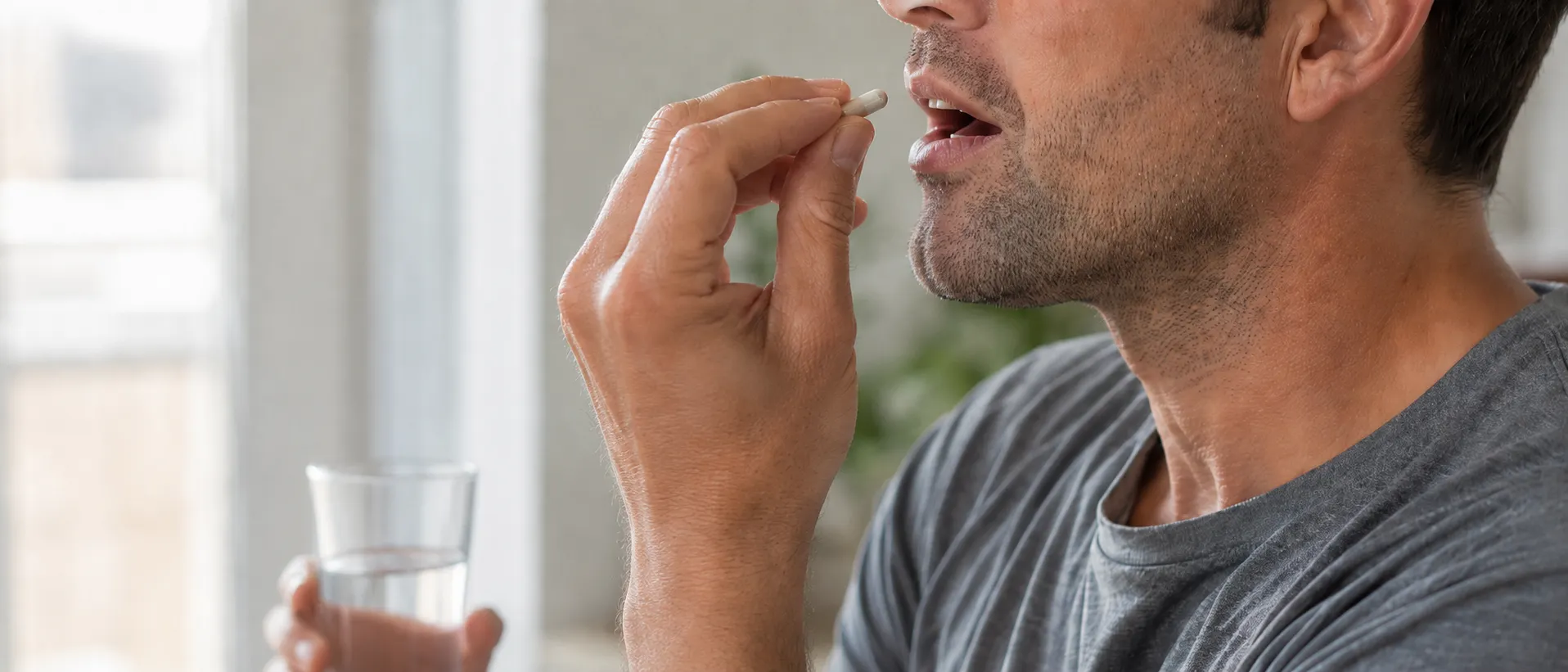 Man taking a capsule with a glass of water, representing daily use of omeprazole or other PPIs for acid reflux.