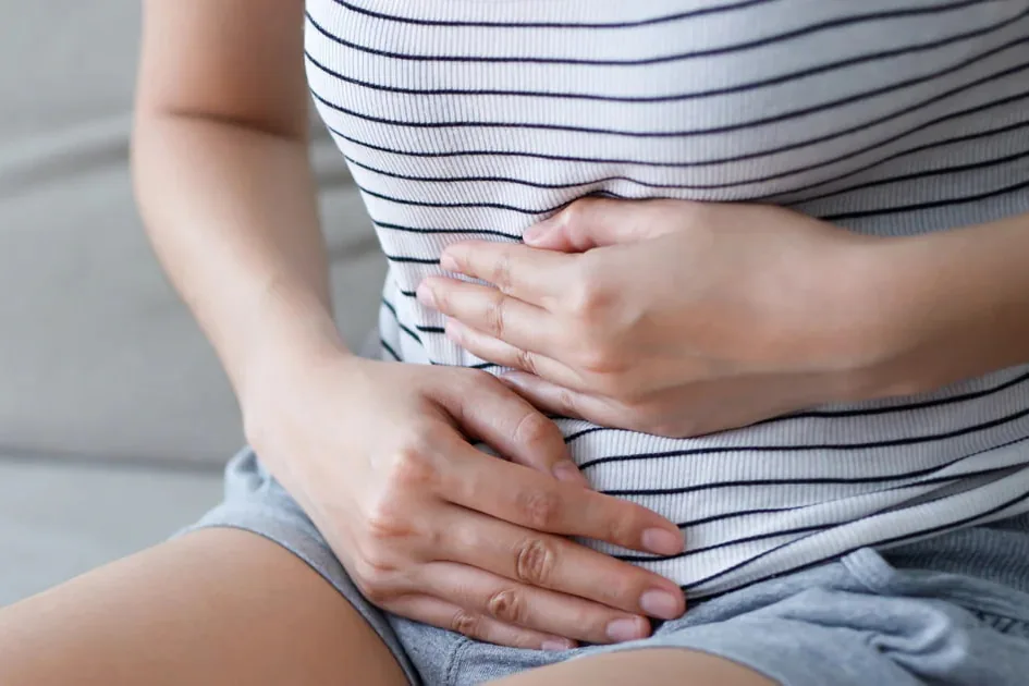 Woman sitting on a sofa holding her stomach with both hands, a common sign of bloating and gut discomfort